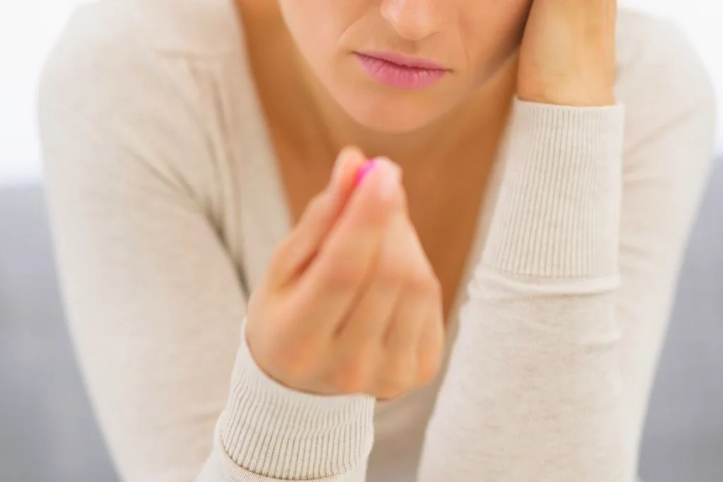 A frustrated person looking at a pill of medication that didn't work for their persistent symptoms.