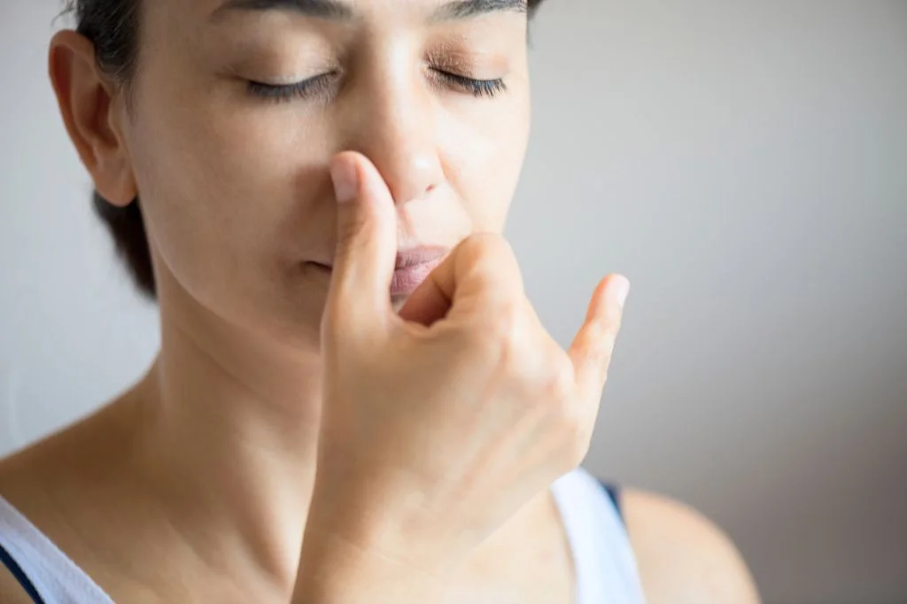 A person testing for a deviated septum by blocking one nostril to check for airflow restriction.