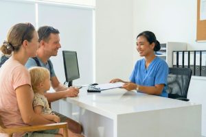 A traveler happily using their insurance card at Hydro Medical Bali's reception desk for cashless ENT treatment.