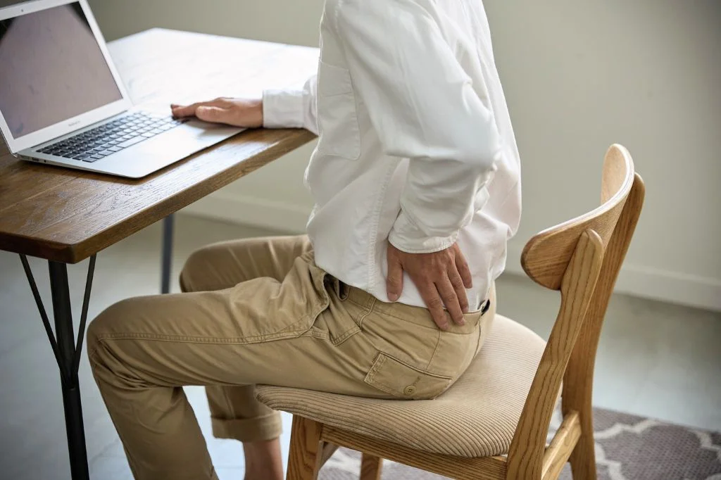 A remote worker in Bali experiencing lower back pain and poor posture from sitting too long at a cafe.