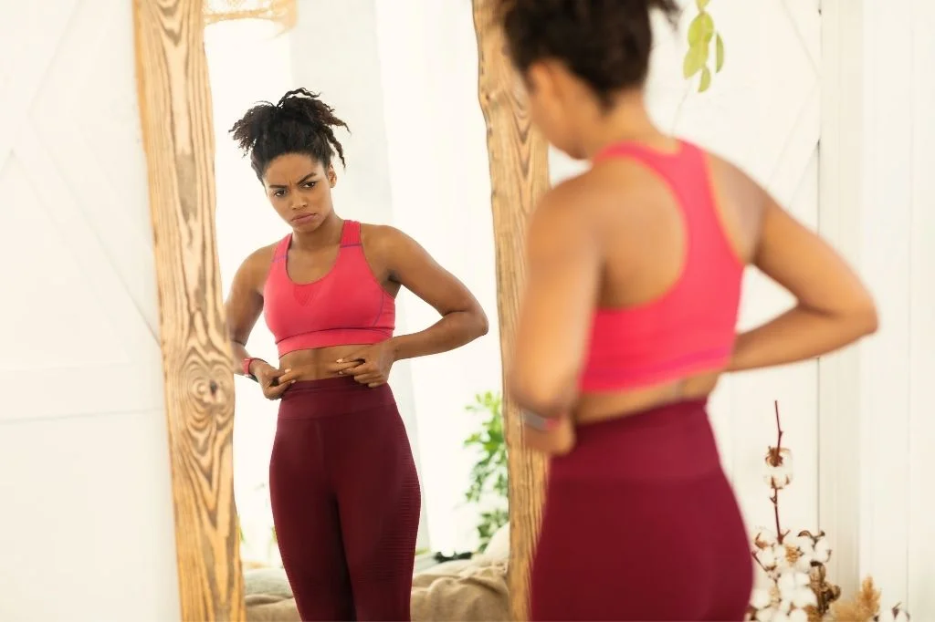 A person in Bali pinching stubborn belly fat, wondering whether fat freezing or muscle toning is the right solution.