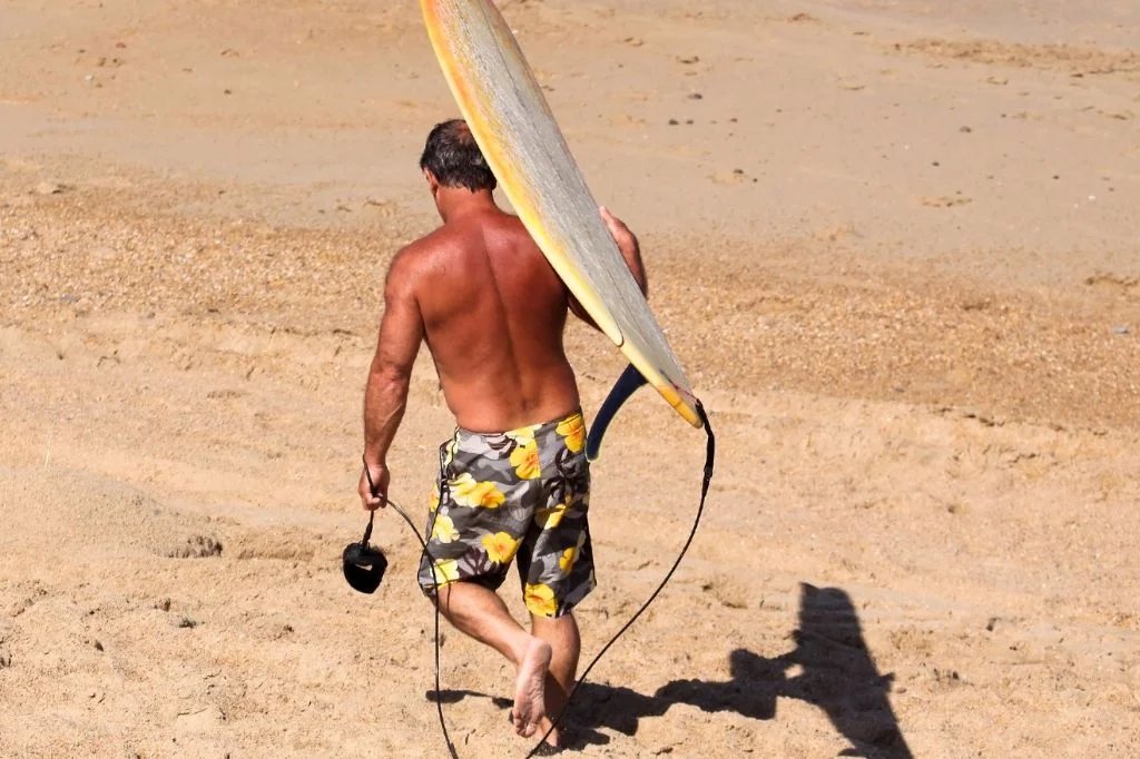 A surfer in Bali holding their surfing board in pain after riding the waves.