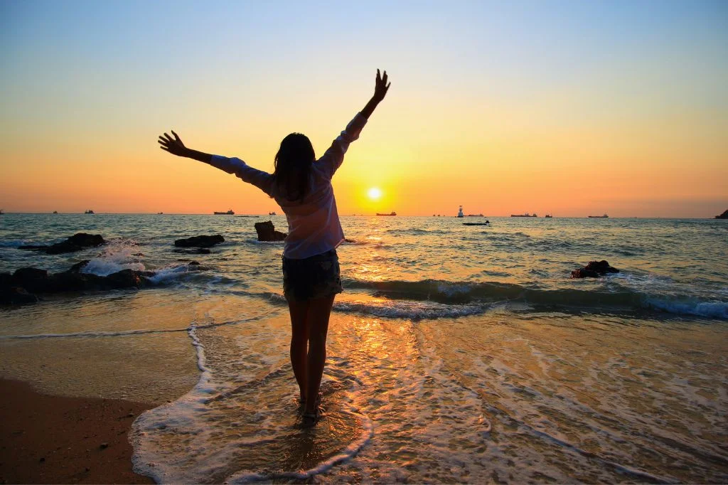 A healthy, pain-free expat stretching and enjoying the sunset on a Bali beach after fixing their posture.